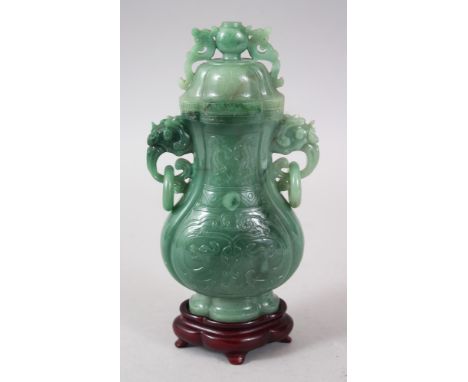 A 20TH CENTURY CHINESE CARVED JADE LIDDED VASE &amp; STAND, the vase with a lion dog handled lid, with twin lion dog handles 