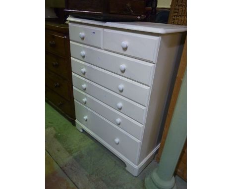 A modern white wood bedroom chest of five long and two short drawers with white button ceramic handles and bracket shaped 