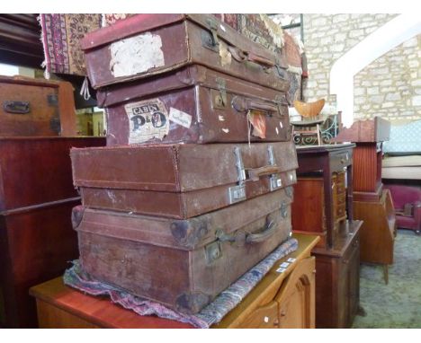 A stack of four vintage leather suitcases of varying size, some with reinforced corners and brass fittings