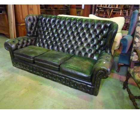 A three seat green leather wing back sofa with buttoned upholstery and loose seat cushions