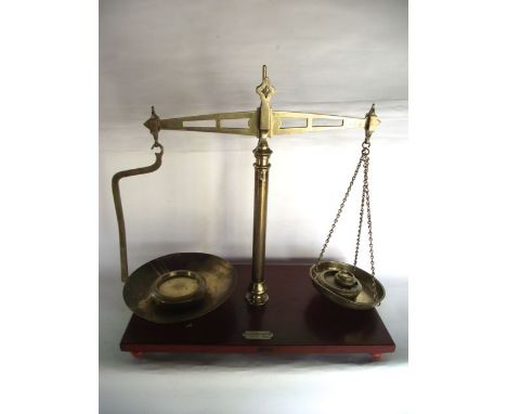 A large beam scale assembly, principally in brass raised on a stained timber base bearing label B & H Bracy Limited, 53 Bridg