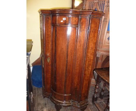 An 18th century freestanding walnut corner cupboard, probably Dutch, with bow front enclosed by a moulded panelled door raise