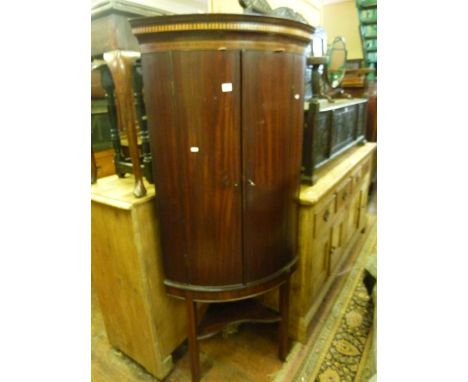 A Georgian mahogany bow fronted corner cupboard with inlaid detail and enclosed by two doors raised on a later stand