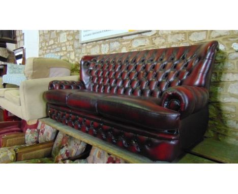 A contemporary ox blood leather upholstered buttoned and wing backed three seat sofa with rolled arms together with a similar