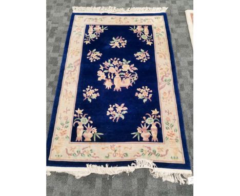 A Peking Oriental rug with precious objects and botanical sprays, on a dark blue ground, with tassels to two ends, 122 x 204c