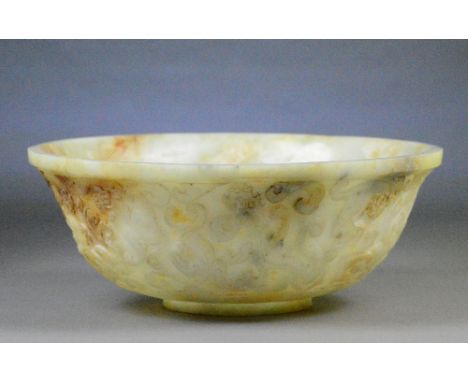 A large Chinese pale celadon and russet included jade bowl decorated to the exterior with chilong within scrolls on short foo