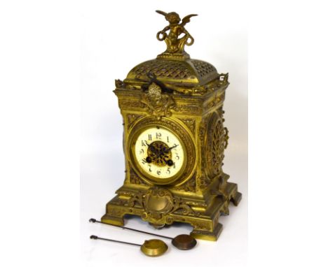 A c.1900 French brass mantel clock with ornate decoration of mask heads, scrolls, and a cupid finial on bracket feet, the ena