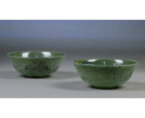 A pair of Chinese spinach jade bowls with etched decoration of a continuous landscape to the exterior of the body, various sc