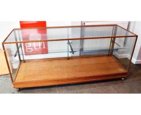 A LARGE SHOPFITTERS DISPLAY CABINET  with interior shelf and sliding glass doors, on casters, 180cm long 60cm deep 81cm high