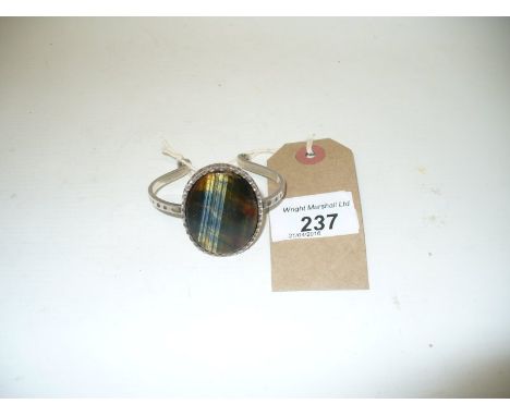A modern silver and polished stone bangle, the polished stone, displaying multi-colours, centrally set to a scalloped surroun