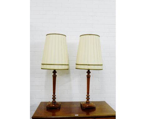 A pair of turned wood table lamp bases on square bases with bun feet complete with pleated shades, length excluding light fit