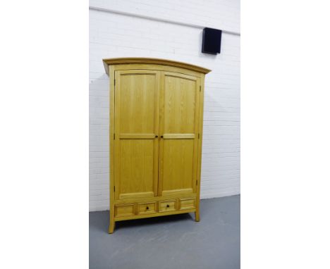 A contemporary light oak wardrobe, the arched top pediment above a pair of panel cupboard doors, fitted with drawers to the b