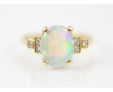 A late 20th century white opal and diamond ring, the central white opal oval cabochon four claw set in yellow metal, with thr