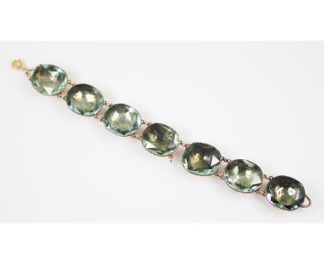 A foiled back paste bracelet, 19th century, the ‘aquamarine’ coloured cushion cut stones set within a yellow metal closed bac