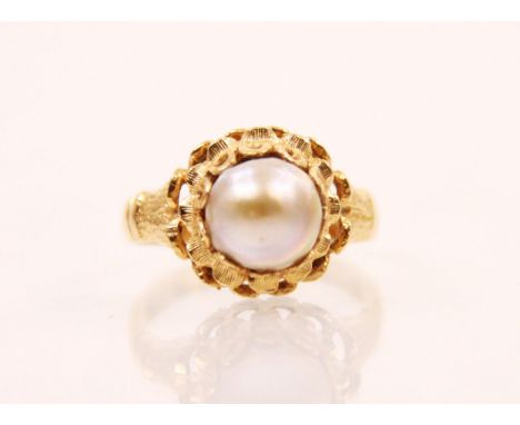 A cultured pearl and yellow metal ring, the central baroque shaped pearl set within an openwork stylised mount with engraved 