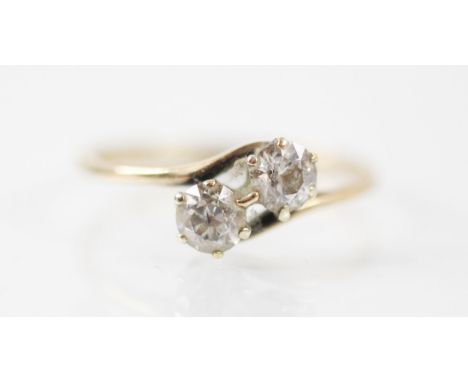 A two stone diamond cross over ring, the round brilliant cut diamonds claw set in yellow metal shank, stamped '18ct' ring siz