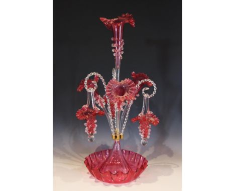 A cranberry glass epergne of typical form, with central trumpet over three lower trumpets, and three canes supporting hanging