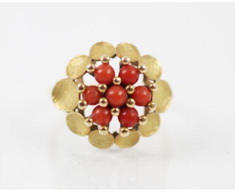 An untested coral and yellow metal dress ring, the seven spherical corals beads designed as a flowerhead with matte out swept