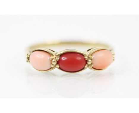 A 9ct yellow gold coral three stone ring, the central red oval coral cabochon with a pink oval coral cabochon to each side, a