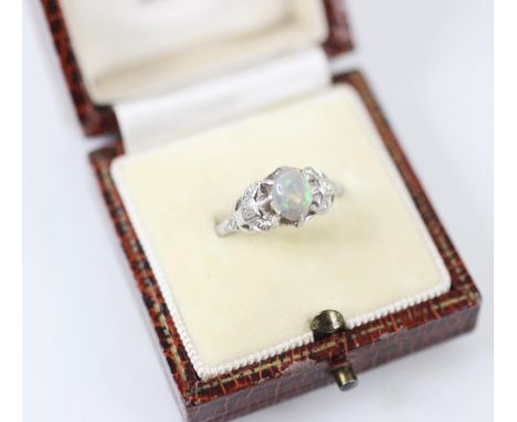 A precious opal and diamond ring, the raised oval opal cabochon claw set in white metal, with baguette and round cut diamond 