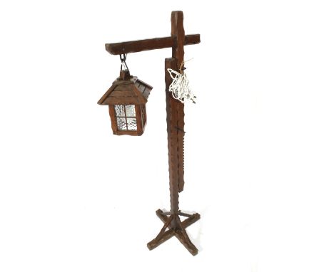 A carved wooden Arts & Crafts style adjustable standard floor lamp. Of lantern form hanging from a gallows type stand. 