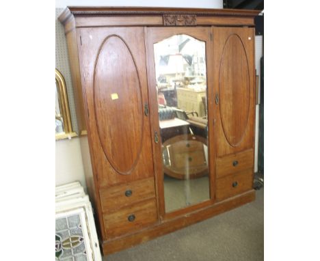 A triple Edwardian mahogany wardrobe. With dentile cormicing over a relief plaque depicting an urn and swags, and central mir