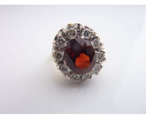 A garnet and diamond ring, centred with an oval mixed-cut untested garnet weighing approximately 3.14cts, within a surround o