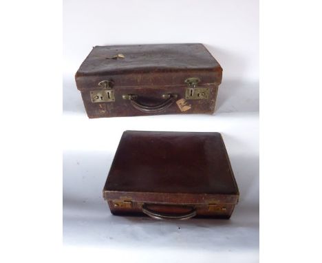 A vintage stitched leather suitcase with metallic lock plates, bearing remnants of travel labels, with simple interior, 45 cm