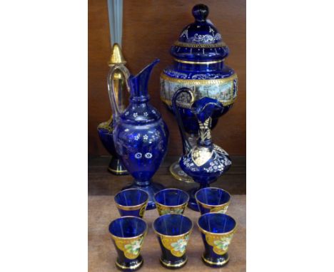 A Bohemian blue glass liqueur set with six glasses, two glass ewers and a lidded glass vase decorated with enamel and transfe