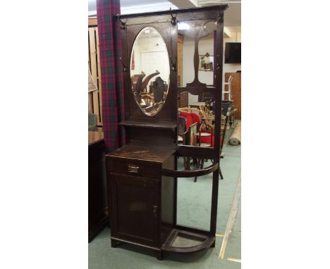 A late Victorian stained oak mirror backed hall stand with oval bevelled glass mirror over single drawer, cabinet door alongs