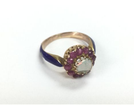 An 18ct gold ring set with a central opal surrounded by rubies and with blue enamelled shoulders. Approx 4.2g and approx size