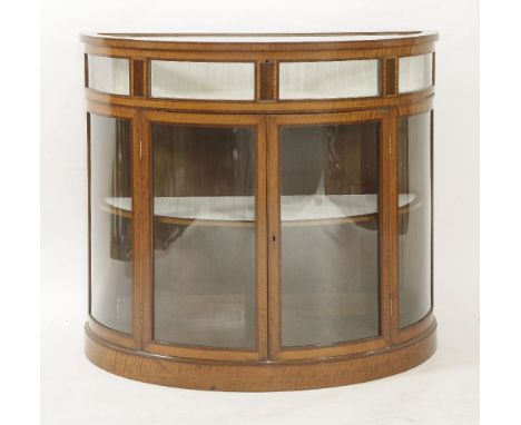 A George III style satinwood and mahogany crossbanded vitrine, of demilune form, the hinged top enclosing a lined cabinet, ov