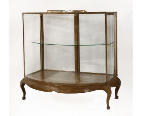 A walnut bow front shop display cabinet,the bevelled glass front enclosing a single shelf, with a pair of doors to the revers