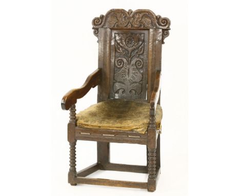 An oak armchair,17th century, with a shaped top rail carved with leaves, the carved panel back with a stylised flower, on bob