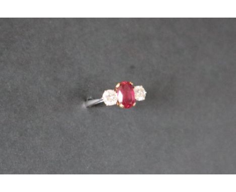 A ruby and diamond ring set with a central oval faceted ruby, approximately 9mm x 6mm,  flanked by a pair of round brilliant 