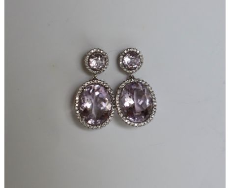 A pair of amethyst and diamond drop earrings, each set with circular and oval faceted amethysts each surrounded by a halo of 