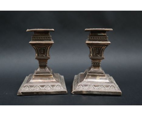 A pair of late Victorian silver desk candlesticks, of square form decorated with swags and flower heads, London, 1893, Charle