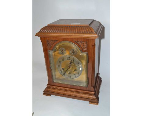 Early 20th Century mantel clock by Jung Hans with arched brass and silver dial, three train brass movement and set in a carve