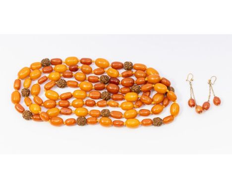 A strand of egg yolk amber type beads, interspersed with carved beads, along with a pair of similar earrings in yellow metal.