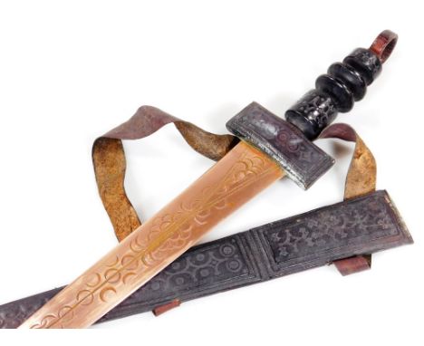 A 20thC African tribal knife, probably Nigerian, with tapering brass blade, turned wooden handle and scabbard, 79cm W.