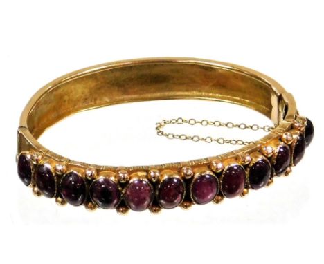 A 9ct gold cabochon set garnet hinged bangle, with design of twelve cabochon cut garnets, safety chain, an etched design, 6.2