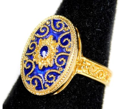 An 18ct gold Eastern enamel dress ring, the ring head of oval form with floral scroll borders and blue enamel, with rope twis