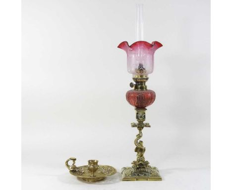 An ornate 19th century brass oil lamp, with a cranberry glass shade, 54cm high overall, together with a brass chamberstick (2