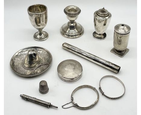A collection of silver items including pill pot, dwarf candlestick, egg cup, child's bangles, continental sombrero etc.