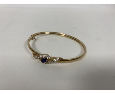 A 9ct gold bangle with central blue stone surrounded by clear paste stones (6cm) (7.84g)