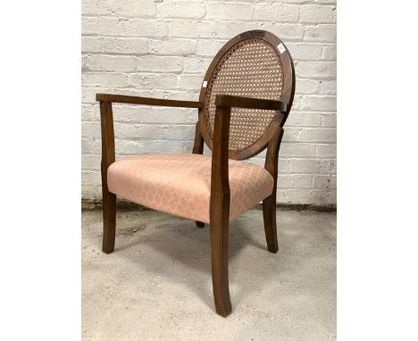 An early 20th century walnut bedroom open armchair, the oval back with cane panel over upholstered seat, raised on square spl