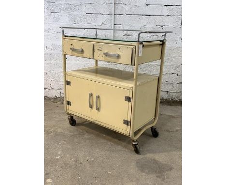 A vintage chrome and cream painted tubular hospital trolley, with plate glass top over two drawers, an open shelf and double 
