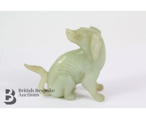 Celadon jade carving of a puppy, seated on her haunches with her head over one shoulder, approx 9 x 9 cms.&nbsp;
