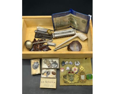 Box of interesting odds to include miniature harmonica, Military cap badges, Three silver fob medals, Three various £1 bank n