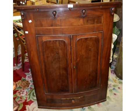 A 19th century bow front mahogany wall mounted corner cupboard, stepped cornice, two raised panel doors over single drawer, b